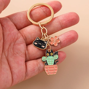 Detail of a gold enamel keychain with a black cat, cherry blossom, and cactus cat charm