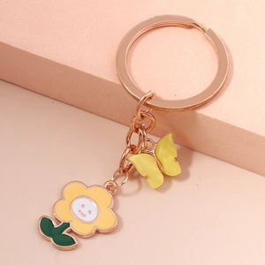 Detail of rose gold keychain with yellow smiley flower and butterfly on pink background
