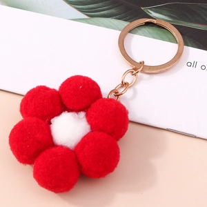 Plush red flower keychain with white center and gold metal ring on a peach desk