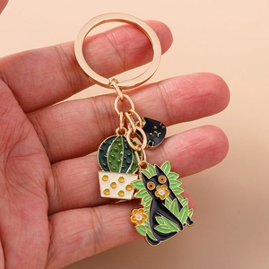 Detail view of cartoon black cat and cactus charms on a golden metal keychain pendant