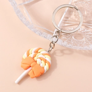 Close-up of spiral orange and yellow lollipop keychain with a bow on soft pink background