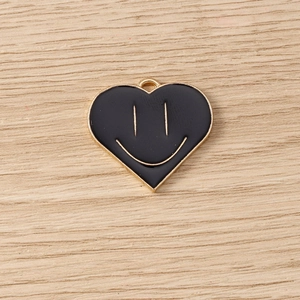 Macro detail of a heart-shaped smiling face pendant in gold alloy with black enamel
