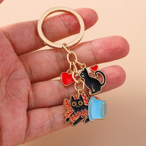 Detail of cute black cat enamel keychain with golden ring and red heart charms on hand
