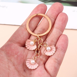 Dettaglio portachiavi dorato con conchiglie in smalto rosa e accenti di perle bianche