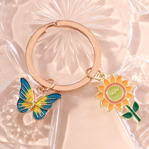 Close-up of golden keychain featuring enamel butterfly and smiling sunflower pendants