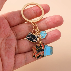 Close-up of golden keychain with enamel black cat and blue cloud charms held by hand
