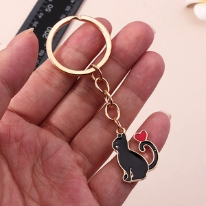 Vue en main d'un porte-clés chat noir émaillé avec cœur rouge et anneau doré brillant