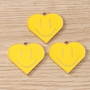 Three yellow heart smiley face charms in enamel alloy for DIY jewelry on wood background
