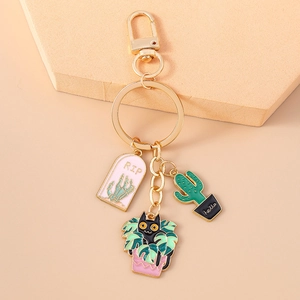 Detail of golden metal keychain with black cat, cactus, and RIP tombstone enamel charms