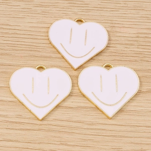 Detailed close-up of golden heart smiley face enamel charms on a light wood background