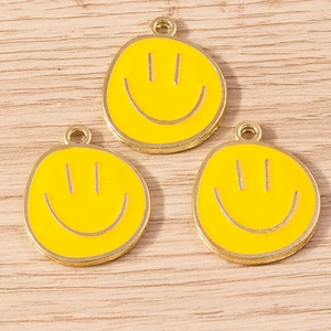 Three yellow smiley face alloy pendants with gold plating on light wood background