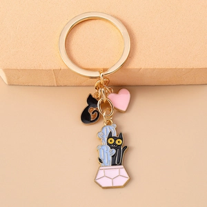 Detail view of golden keychain with enamel black cat and pink heart charms on soft background