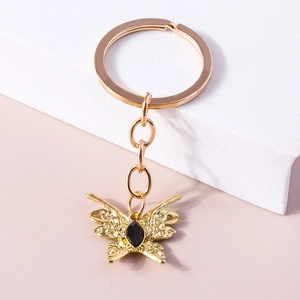 Golden butterfly keychain with black gemstone pendant on a minimalist background