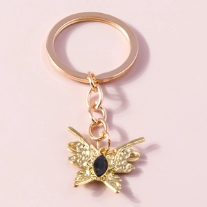 Baroque golden butterfly keychain with black gemstone inlay on a pink background