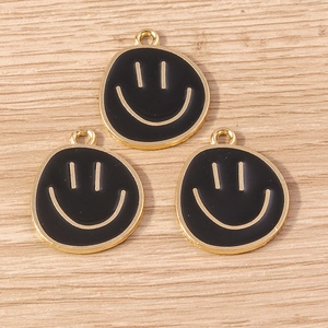 Three black enamel smiley face charms with gold metal edges on a light wooden background