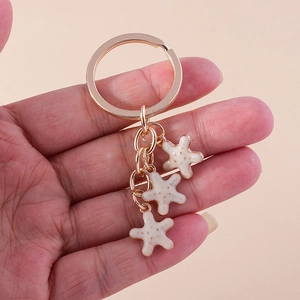 Détail d'un porte-clés doré tenu en main avec trois pendentifs étoiles de mer crème