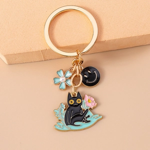 Detail of a golden keychain with a black cartoon cat, blue flower, and smiley face charms