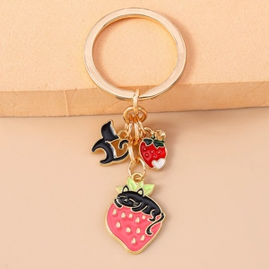 Close-up of golden keychain with cute black cat and strawberry enamel pendants for backpack