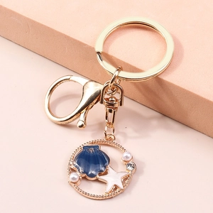 Dettaglio portachiavi stella marina dorata con smalto blu e perla su gradini rosa