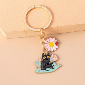 Detail of enamel black cat and pink daisy keychain with gold-plated finish on beige block