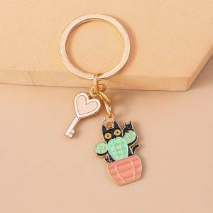 Detailed close-up of a gold keychain featuring a black cat cactus and white heart key charm