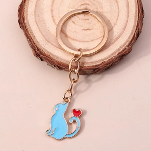 Gros plan d'un porte-clés doré avec pendentif chat bleu et cœur rouge sur bois