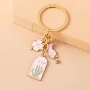 Detail of gold metal keychain with pink cat, clover, and RIP headstone charms