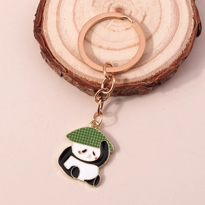 Porte-clés panda avec anneau or rose et chapeau de paille sur un fond rose doux