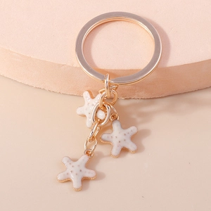 Détails du porte-clés étoile de mer dorée avec breloques en émail blanc sur fond doux