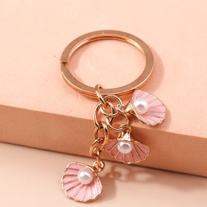 Dettaglio di un portachiavi in oro rosa con tre conchiglie rosa e perle bianche