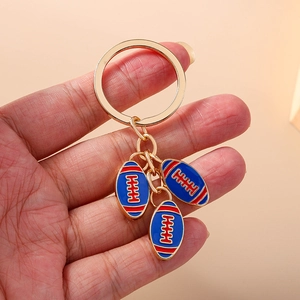 Portachiavi rugby dorato con ciondoli in smalto blu tenuto in mano su sfondo arancio