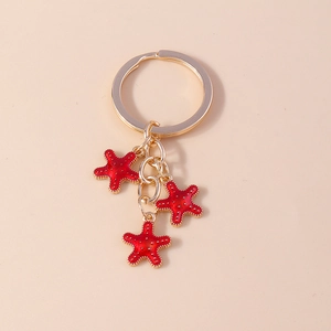 Détail d'un porte-clés doré avec trois breloques étoiles de mer rouges à points blancs