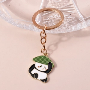 Gros plan d'un porte-clés panda avec chapeau vert et anneau en or rose sur fond rose doux