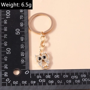 Detail view of gold owl keychain with rhinestones showing weight of 6.5g on a scale