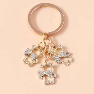 Close-up of golden hollow bear keychains with colorful rhinestone bows on a pink background