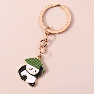 Détail d'un porte-clés panda en or rose avec chapeau vert sur fond rose texturé élégant