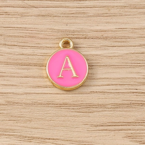 Detailed shot of pink enamel gold-plated round charm with letter A on wood background