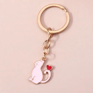Détail du porte-clés chat en or rose avec émail rose et breloque coeur rouge sur fond rose
