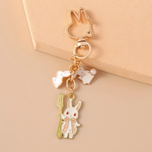 Détail d'un porte-clés lapin en émail avec pendentifs dorés sur une surface beige doux