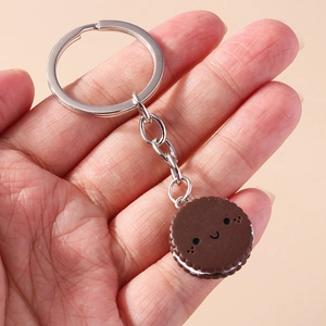 Cartoon chocolate sandwich cookie keychain with smiling face held in hand on beige background