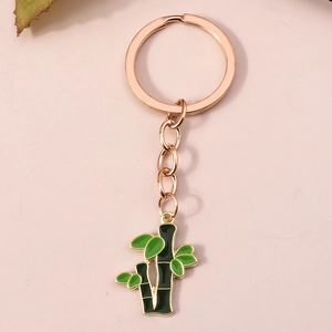 Détail d'un porte-clés en or rose avec bambou et feuilles vertes sur fond rose