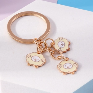 Detail of cute gold keychain with three cartoon sheep pendants on white display surface
