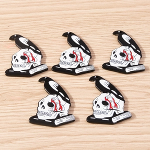 Gothic acrylic charms with crow and skull on books, flat lay on light wood background