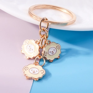 Detail of three cute enamel sheep charms on a gold metal keychain for DIY backpack decor