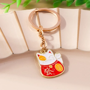 Detail of a lucky cat keychain with golden finish and red enamel on a ceramic tray