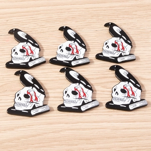 Macro view of 6 gothic raven and skull resin charms with holes on a light wood background