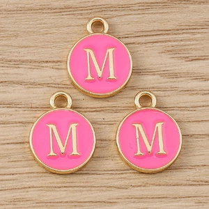 Detail of pink enamel letter M charms with gold plating and hanging loop on wood