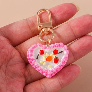 Close-up of a pink heart cake keychain with strawberry and cherry resin details