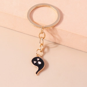 Close-up of golden metal keychain with black enamel ghost pendant on geometric blocks