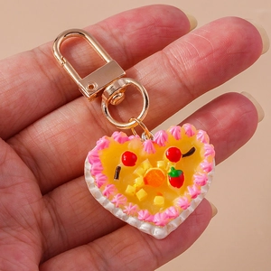 Handheld heart-shaped dessert keychain with yellow cake, fruit toppings and golden clasp